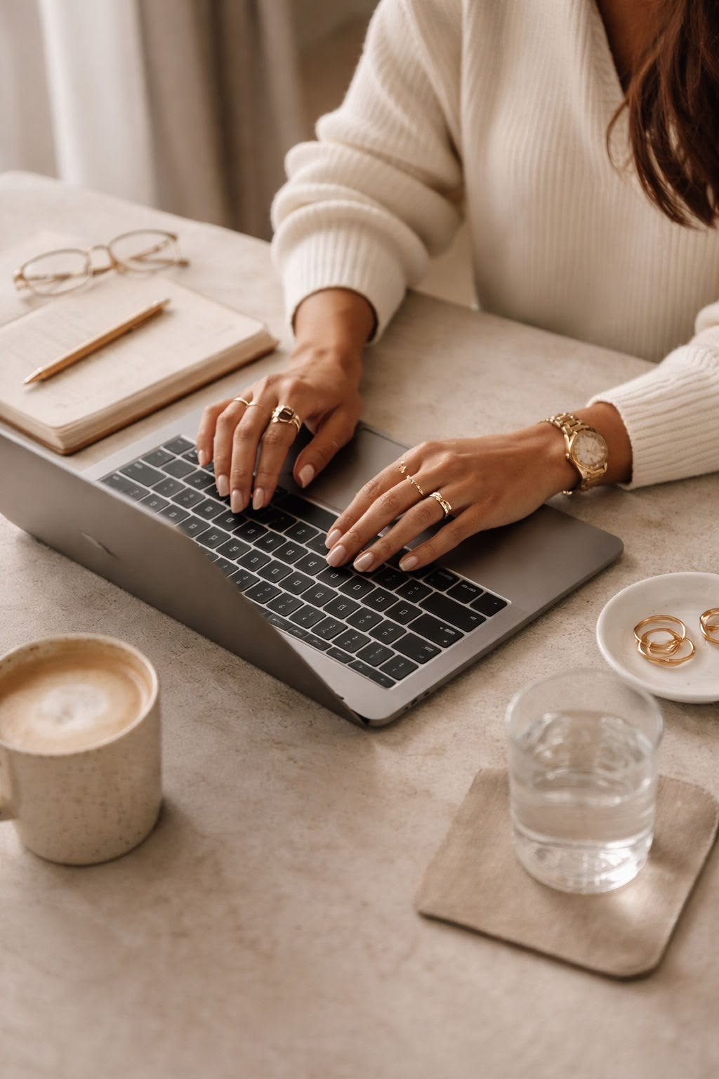 Hände tippen auf einem Laptop neben Notizbuch, Brille und Kaffee – Recherche beim Location Scouting für eine Hochzeit