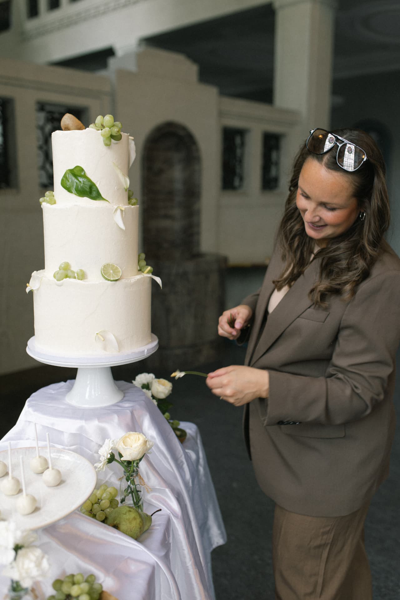 Vivien Opoku richtet die letzten Details einer dreistöckigen Hochzeitstorte mit Limettenscheiben, Trauben und Blättern auf einer Desserttafel her