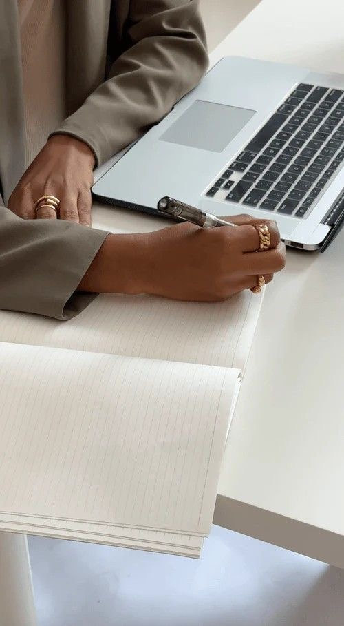 Hand notiert mit Stift in einem Notizbuch neben einem geöffneten Laptop – Recherche für die Hochzeitslocation Beratung