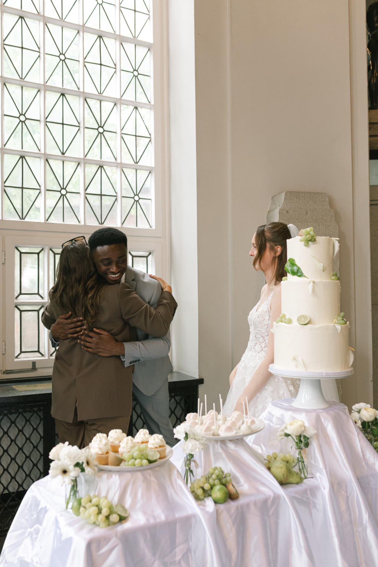 Der Bräutigam umarmt Vivien Opoku neben einer dreistöckigen Hochzeitstorte und einer reich gedeckten Desserttafel, die Braut steht daneben