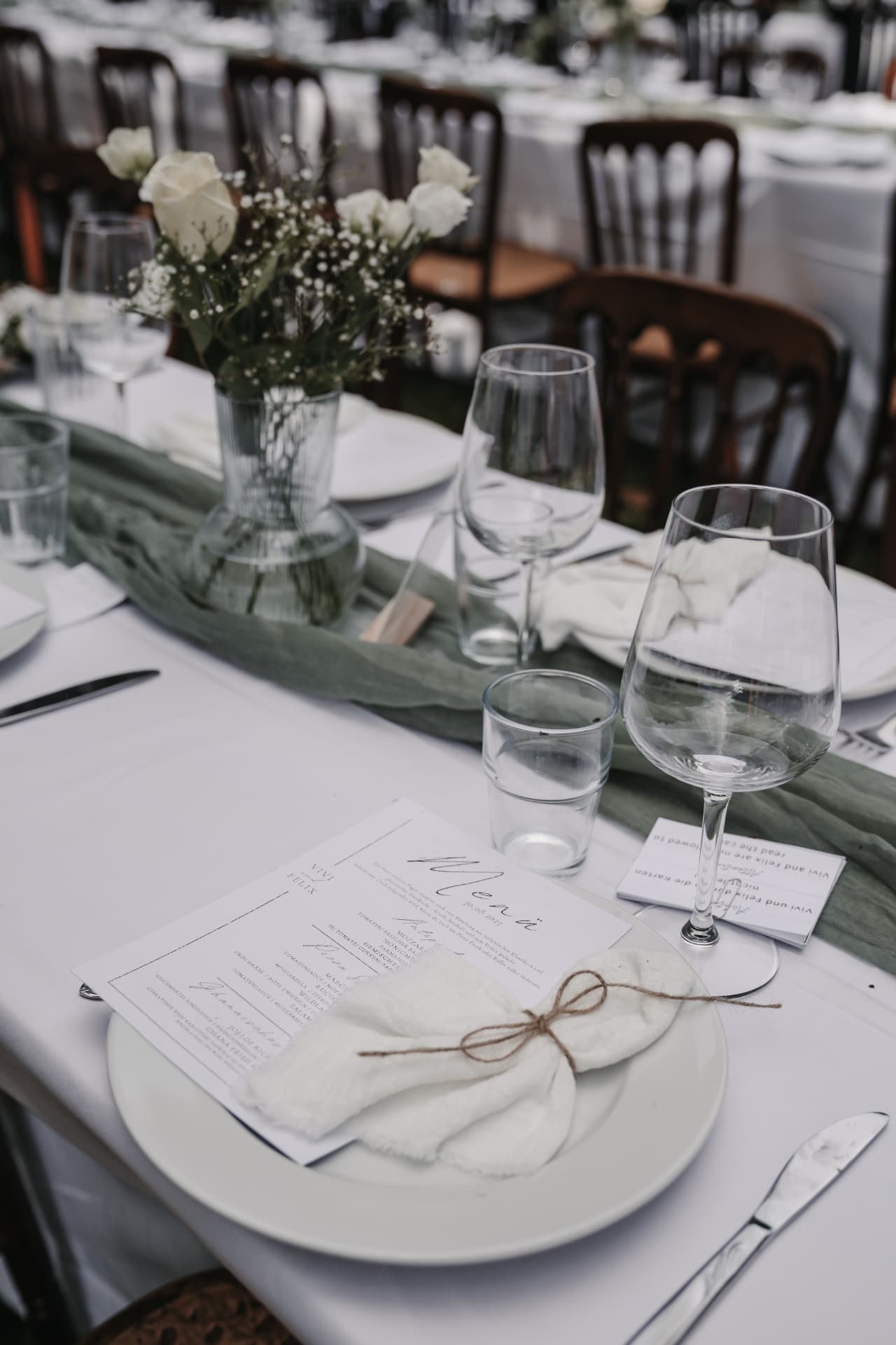 Festlich gedeckte Tafel mit Menükarte, weißer Stoffserviette, Wein- und Wasserglas und weißen Rosen