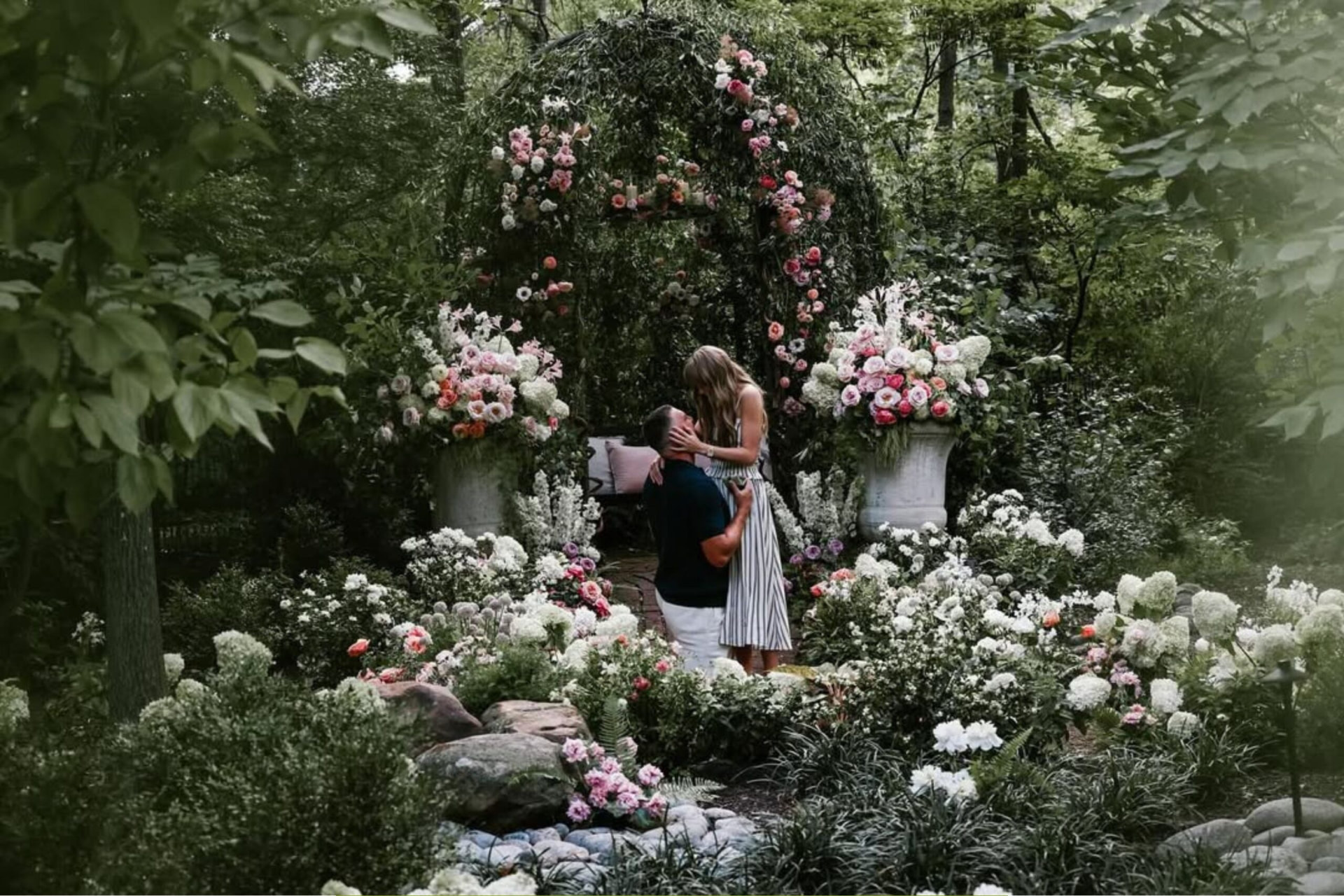 Taylor Swift und Travis Kelce bei ihrer Verlobung in einem blühenden Garten vor einem mit Rosen bewachsenen Laubengang